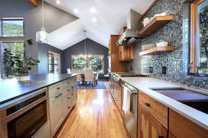 Kitchen with open shelves, vaulted ceiling, island range hood, light wood-type flooring, and backsplash