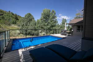 View of swimming pool with a deck, outdoor dining area, and view of scattered trees
