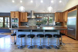 Kitchen with dark countertops, stainless steel appliances, vaulted ceiling, brown cabinets, and a spacious island