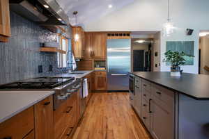 Kitchen featuring appliances with stainless steel finishes, dark countertops, light wood-type flooring, range hood, and open shelves