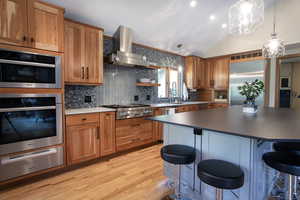 Kitchen with a warming drawer, light wood finished floors, stainless steel appliances, a kitchen bar, and wall chimney exhaust hood