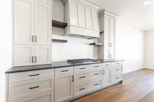 Kitchen featuring tasteful backsplash, wood finished floors, dark countertops, custom range hood, and stainless steel gas stovetop