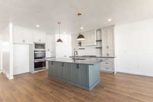 Kitchen with dark countertops, dark wood-type flooring, recessed lighting, a center island with sink, and white cabinetry