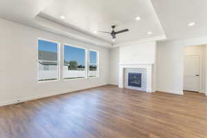 Unfurnished living room with a raised ceiling, ceiling fan, wood finished floors, a tiled fireplace, and recessed lighting