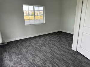 Empty room featuring baseboards and dark colored carpet