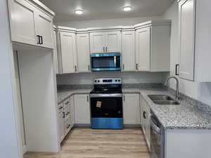 Kitchen featuring stainless steel appliances, light stone counters, light wood finished floors, and white cabinets