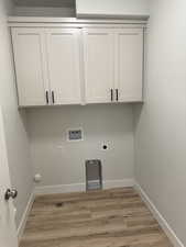 Laundry area featuring light wood-type flooring, hookup for a washing machine, electric dryer hookup, and cabinet space