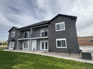 Rear view of house featuring french doors, a balcony, a yard, and brick siding