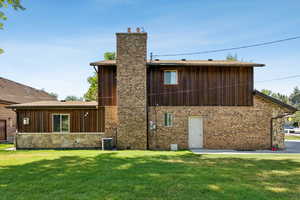 Rear view of property with a chimney, a lawn, brick siding, and board and batten siding