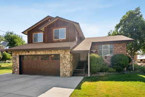 View of front facade featuring stone siding, a garage, and roof with shingles