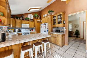 Kitchen with tile counters, white appliances, backsplash, a peninsula, and glass insert cabinets