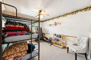 Carpeted bedroom featuring wallpapered walls, a textured ceiling, a wainscoted wall, and a ceiling fan