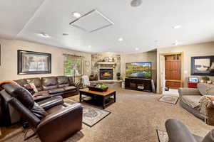 Carpeted living area with recessed lighting, a stone fireplace, and attic access