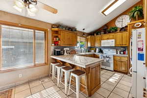 Kitchen featuring tile counters, a peninsula, light tile patterned floors, vaulted ceiling, and white appliances