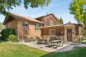 Rear view of house with a yard, board and batten siding, brick siding, a patio area, and roof with shingles