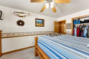 Bedroom with wallpapered walls, carpet floors, a closet, a ceiling fan, and a wainscoted wall