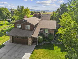 View of front of house with stone siding, an attached garage, roof with shingles, a chimney, and concrete driveway