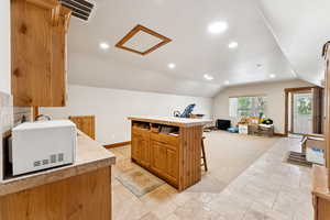 Kitchen featuring white microwave, vaulted ceiling, light countertops, a kitchen bar, and recessed lighting