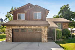 View of front of house with stone siding, driveway, and roof with shingles