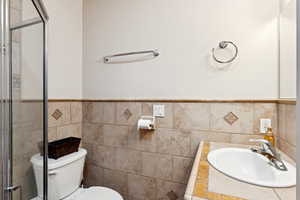 Bathroom featuring a stall shower, vanity, tile walls, and wainscoting