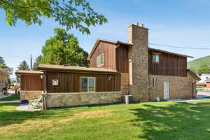 Rear view of house with board and batten siding, a chimney, a lawn, and brick siding