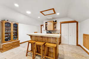 Kitchen featuring open shelves, light countertops, a kitchen breakfast bar, backsplash, and vaulted ceiling