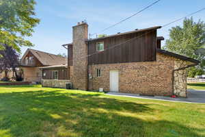 Back of house with a chimney, a lawn, and brick siding