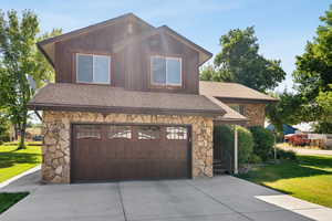 View of front of property with stone siding, roof with shingles, and concrete driveway