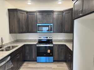 Kitchen featuring stainless steel appliances, light wood-style flooring, light stone countertops, dark brown cabinets, and a textured ceiling
