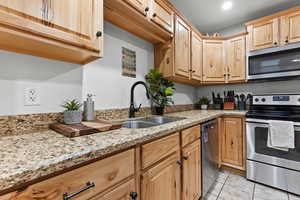 Kitchen with appliances with stainless steel finishes, light stone counters, light tile patterned floors, and light brown cabinets