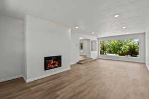 Unfurnished living room with wood finished floors, a textured ceiling, a glass covered fireplace, and recessed lighting
