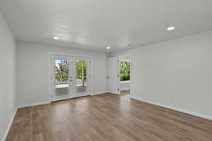 Empty room with french doors, wood finished floors, a textured ceiling, and recessed lighting