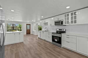 Kitchen with stainless steel appliances, a textured ceiling, light countertops, decorative backsplash, and glass insert cabinets