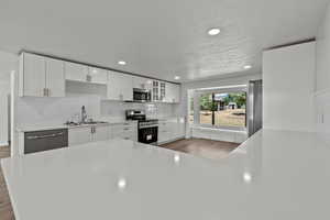 Kitchen featuring appliances with stainless steel finishes, white cabinetry, light countertops, a textured ceiling, and decorative backsplash