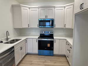 Kitchen featuring appliances with stainless steel finishes, white cabinets, light stone counters, and light wood-type flooring