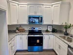 Kitchen with stainless steel appliances, white cabinetry, light stone counters, and dark wood-style flooring