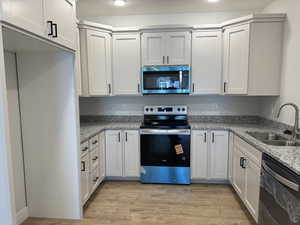 Kitchen featuring appliances with stainless steel finishes, light stone countertops, and white cabinetry