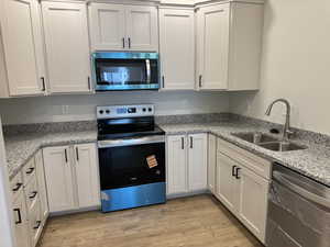Kitchen featuring appliances with stainless steel finishes, light stone counters, and white cabinetry
