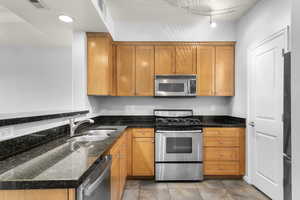 Kitchen with stainless steel appliances, dark stone counters, and brown cabinets
