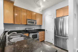 Kitchen with stainless steel appliances, brown cabinets, and dark stone counters