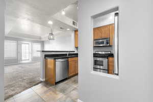 Kitchen featuring light carpet, stainless steel appliances, a textured ceiling, brown cabinetry, and a raised ceiling