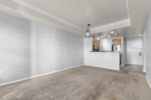 Unfurnished living room with light carpet, recessed lighting, crown molding, a tray ceiling, and light tile patterned floors