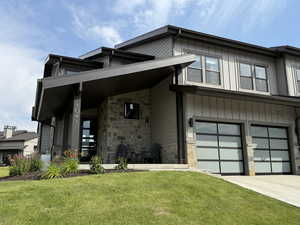 View of front facade with stone siding, a front lawn, driveway, and a garage