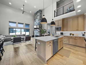 Kitchen featuring open floor plan, light brown cabinets, ceiling fan, a high ceiling, and light wood-style floors