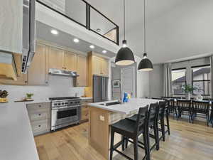 Kitchen with light brown cabinetry, recessed lighting, premium appliances, light countertops, and light wood-style floors