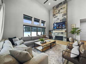 Living room with a towering ceiling, ceiling fan, a stone fireplace, and wood finished floors