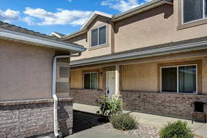 Entrance to property with stucco siding, brick siding, and a porch