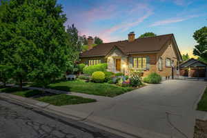 View of front of home featuring concrete driveway, a chimney, a tile roof, brick siding, and a front lawn
