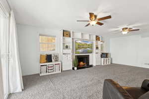 Carpeted living room with ceiling fan and a fireplace with flush hearth