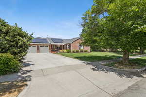 Ranch-style house featuring an attached garage, driveway, a front lawn, solar panels, and brick siding